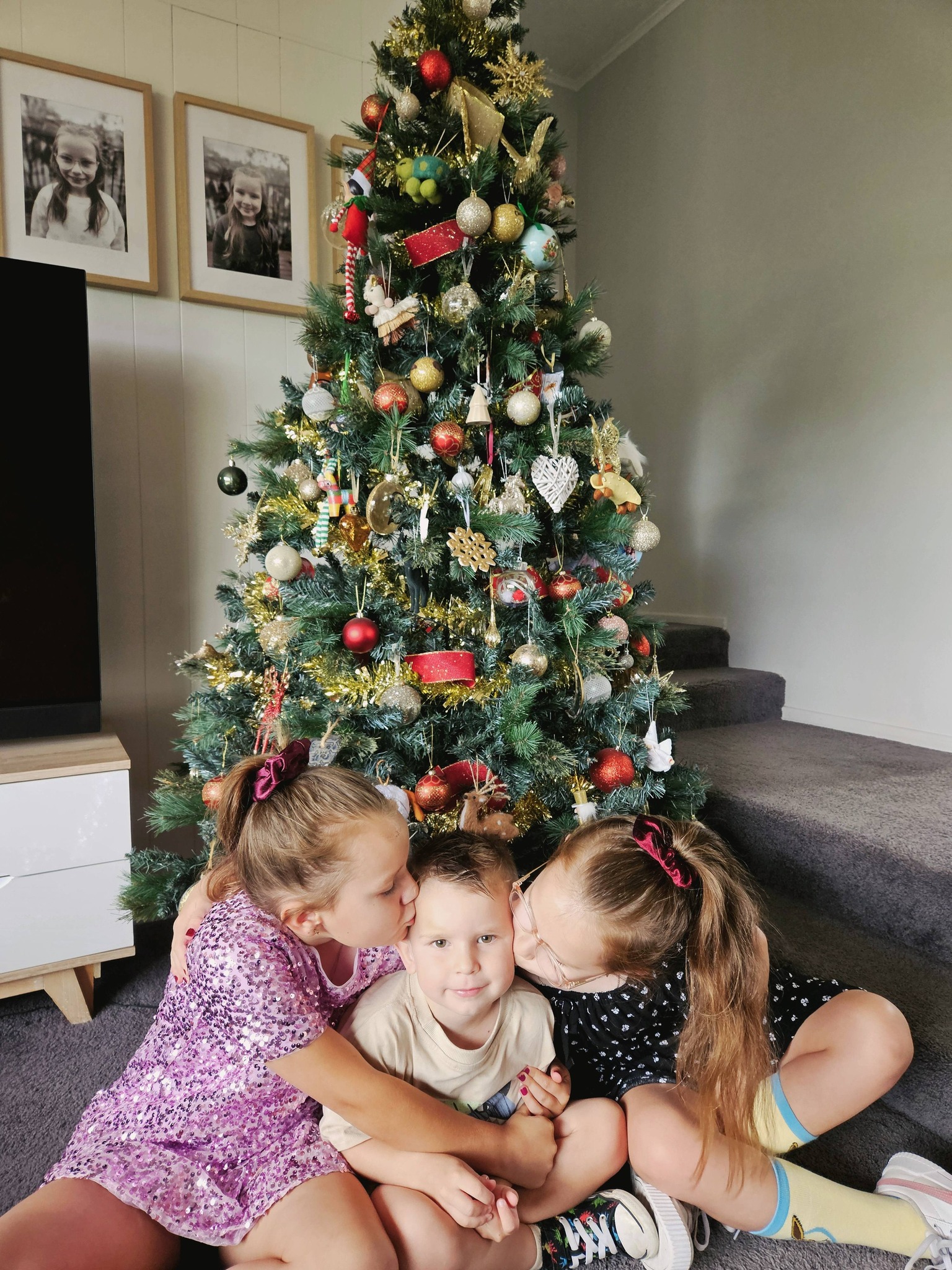 Leon with his sisters in front of a Christmas tree